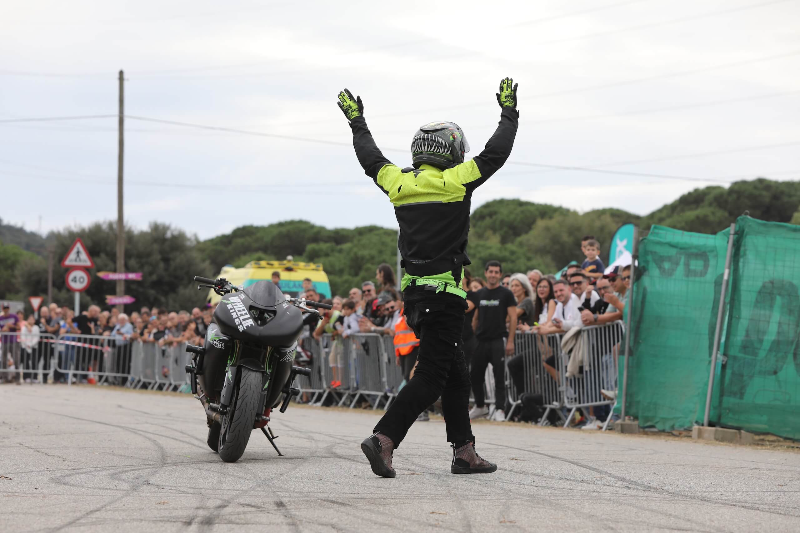 Wheelie desde ángulo bajo mostrando destreza técnica y público de fondo