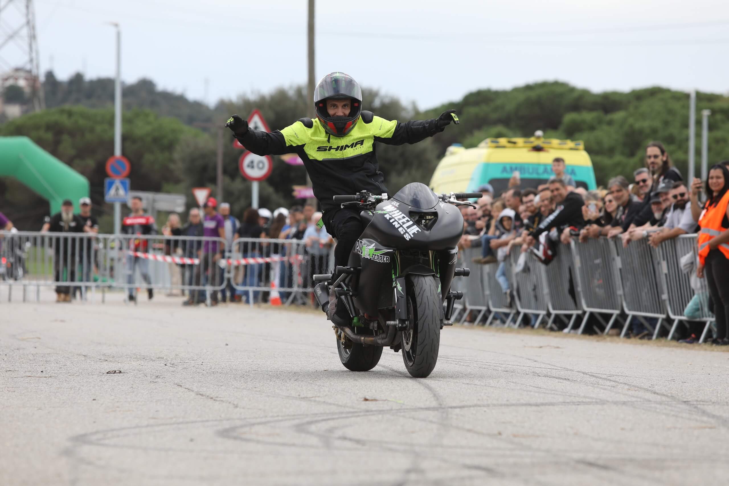 Wheelie con brazos abiertos en zona amplia con público a distancia segura